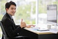 Asian young handsome black short hair happy successful male businessman worker in formal suit sit smile hold thumb up when work Royalty Free Stock Photo
