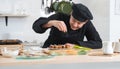 Asian young handsome chef man, in black uniform, smiling while garnishing seaweed on japanese food called takoyaki in kitchen Royalty Free Stock Photo