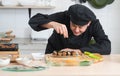 Asian young handsome chef man, in black uniform, smiling while garnishing seaweed on japanese food called takoyaki in plate at kit Royalty Free Stock Photo