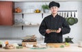 Asian young handsome chef man, in black uniform, smiling and holding on japanese food called takoyaki in plate at kitchen Royalty Free Stock Photo