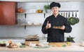 Asian young handsome chef man, in black uniform, smiling thumbs up and holding on japanese food called takoyaki in plate at kitche Royalty Free Stock Photo
