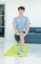 Asian young handsome fit male athlete teenager in sportswear sneakers standing smiling on yoga mat floor stretching legs warming