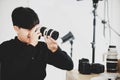Asian young handsome happy male short black hair photographer hold and inspect big DSLR camera lens in hands sit on chair in Royalty Free Stock Photo