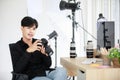 Asian young handsome happy male short black hair photographer wears long sleeve shirt and jeans hold big DSLR camera in hands sit Royalty Free Stock Photo