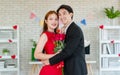 Asian young handsome male boyfriend in formal black suit and beautiful female girlfriend in red dress standing smiling holding red Royalty Free Stock Photo