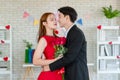 Asian young handsome male boyfriend in formal black suit and beautiful female girlfriend in red dress standing smiling holding red Royalty Free Stock Photo