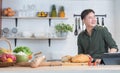 Asian young handsome 30s man sitting, smiling, enjoy cooking in modern kitchen, using tablet while preparing breakfast with bread Royalty Free Stock Photo