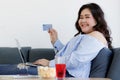 Asian young happy beautiful fat chubby female shopper sit relaxing on sofa smiling at camera hold blue credit card on hand while Royalty Free Stock Photo