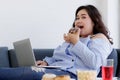 Asian young happy beautiful fat female shopper sit relaxing on fabric sofa look at camera using laptop computer searching products Royalty Free Stock Photo