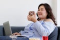 Asian young happy beautiful fat female shopper sit relaxing on fabric sofa look at camera using laptop computer searching products Royalty Free Stock Photo