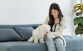 Asian young happy cheerful female owner sitting smiling on cozy sofa couch playing fetching blue ball with best friend small Royalty Free Stock Photo