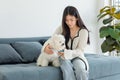 Asian young happy cheerful female owner sitting smiling on cozy sofa couch playing fetching blue ball with best friend small Royalty Free Stock Photo