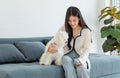 Asian young happy cheerful female owner sitting smiling on cozy sofa couch playing fetching blue ball with best friend small Royalty Free Stock Photo