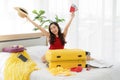 Asian young happy female traveler sitting on bed holding big hat and passport with air tickets overhead sitting look at camera Royalty Free Stock Photo