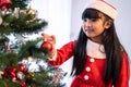 Asian young happy girl kid wear Santa hat and decorate Christmas tree. Young little adorable child wearing red cloth feel excited Royalty Free Stock Photo
