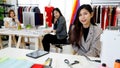 Asian young happy pretty successful female stylish fashion designer sit smiling look at camera at work desk in studio workshop Royalty Free Stock Photo