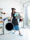 Asian young housewife use detergent and softener with washing machine for clean t-shirt clothes while holding towel basket routine Royalty Free Stock Photo