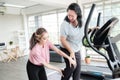 Asian young lady trainer helping senior old lady having knee sprain or injury while workout or running on treadmill in gym.