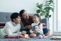 Asian young LGBTQ gay couple giving gift to little Caucasian adopted kid in living room at home. Kid smiling and delighted Royalty Free Stock Photo
