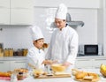 Asian young little boy pastry chef in white uniform with tall cook hat standing while male cooking teacher smiling help teaching