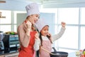 Asian young little cute girl chef daughter wears white tall cook hat and apron standing smiling posing holding fist up celebrating Royalty Free Stock Photo