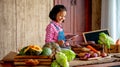 Asian young little girl with smiling use tablet to check the list of various vegetable on table in the kitchen