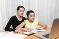Asian young little girl using pencil to do homework with her mother. Student kid writing homework book. Girl use computer to