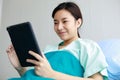 Asian young long hair happy healthy female patient wears green hospital uniform covered by blanket sit lean on blue pillow on bed