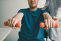 Asian young male physiotherapist helping patient with lifting dumbbells exercises in office