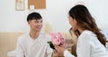 Asian young man kneeling and giving a bouquet of pink flowers to his girlfriend