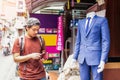 Asian young man looking money in wallet and standing near blue suit in retail store.