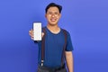 Asian young man showing blank smartphone screen with hand to camera on purple background