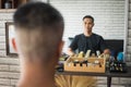 Young man sitting on chair and looking himself in mirror after finished haircut in barbershop