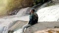 Asian young man, sitting with his backpack, sitting on the edge of a large rock, enjoying the wind and watching nature by the