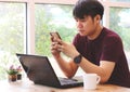 Asian young man sitting by the window in coffee shop with computer laptop on the table Royalty Free Stock Photo