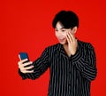 Asian young man touching face and holding smartphone on right hand to take photo by himself or selfie with front smartphone camera Royalty Free Stock Photo