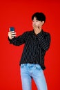 Asian young man touching face and holding smartphone on right hand to take photo by himself or selfie with front smartphone camera Royalty Free Stock Photo