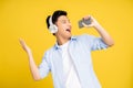 Asian young man wearing headphones and singing favorite on a yellow studio background. He is very happy