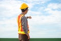 Asian young man worker wearing hard hat and protective vest standing look the cloud and points his finger to side Royalty Free Stock Photo