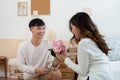 Asian young man kneeling and giving a bouquet of pink flowers to his girlfriend