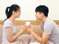 Asian young man and woman holding coffee cup on the bed. The lover smile and look at each other face happily Royalty Free Stock Photo