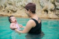 Asian young mother and adorable curly little baby girl having fun in a swimming pool Royalty Free Stock Photo