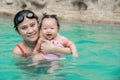 Asian young mother and adorable curly little baby girl having fun in a swimming pool Royalty Free Stock Photo
