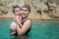 Asian young mother and adorable curly little baby girl having fun in a swimming pool Royalty Free Stock Photo