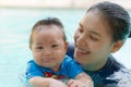 Asian young mother and adorable curly little baby girl having fun in a swimming pool Royalty Free Stock Photo