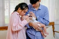 Asian young mother kiss her little baby drink milk from bottle and is held by his father and they stand in living room with soft Royalty Free Stock Photo