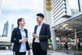 Asian young office businesspeople stand outdoor in city with confident. Formal working partner man and woman hold cup of coffee, f