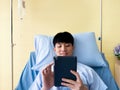 Asian young patient man reading ebook on tablet while recovery body with saline drip and lie down on bed in hostpital Royalty Free Stock Photo