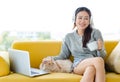 Asian young pretty cheerful female teenager girl in sweater hold coffee cup sitting on sofa smiling playing cuddling with little Royalty Free Stock Photo