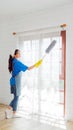 Asian young professional cleaning service woman worker working in the house. The girl cleans the curtain and window. Royalty Free Stock Photo